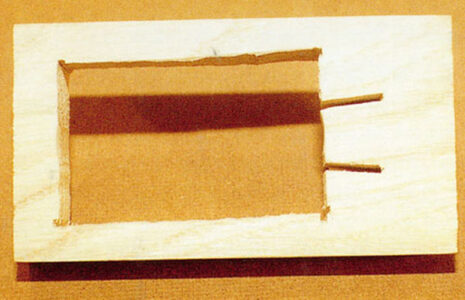 wood board with a rectangular hole cut out of it with two notches cut through on one end